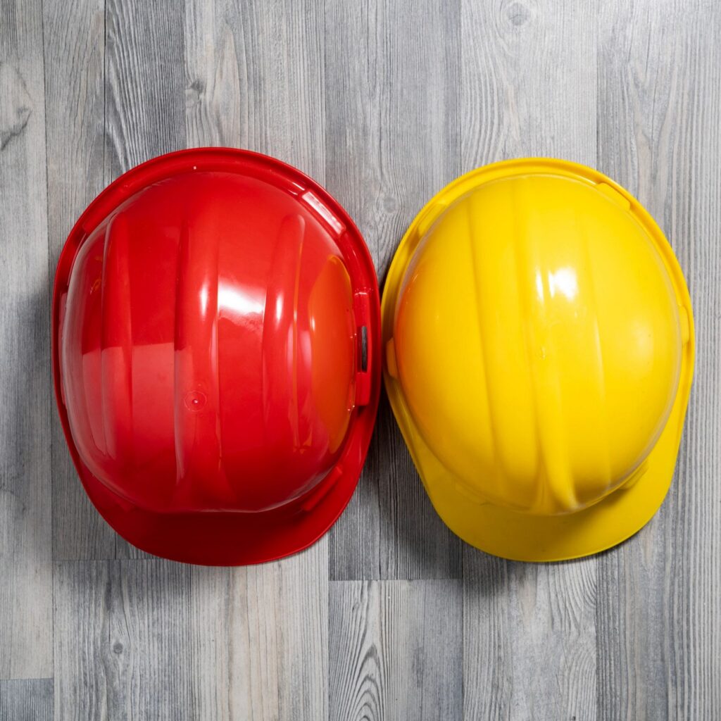 Close up photo of red and yellow colored work helmets on gray wooden background